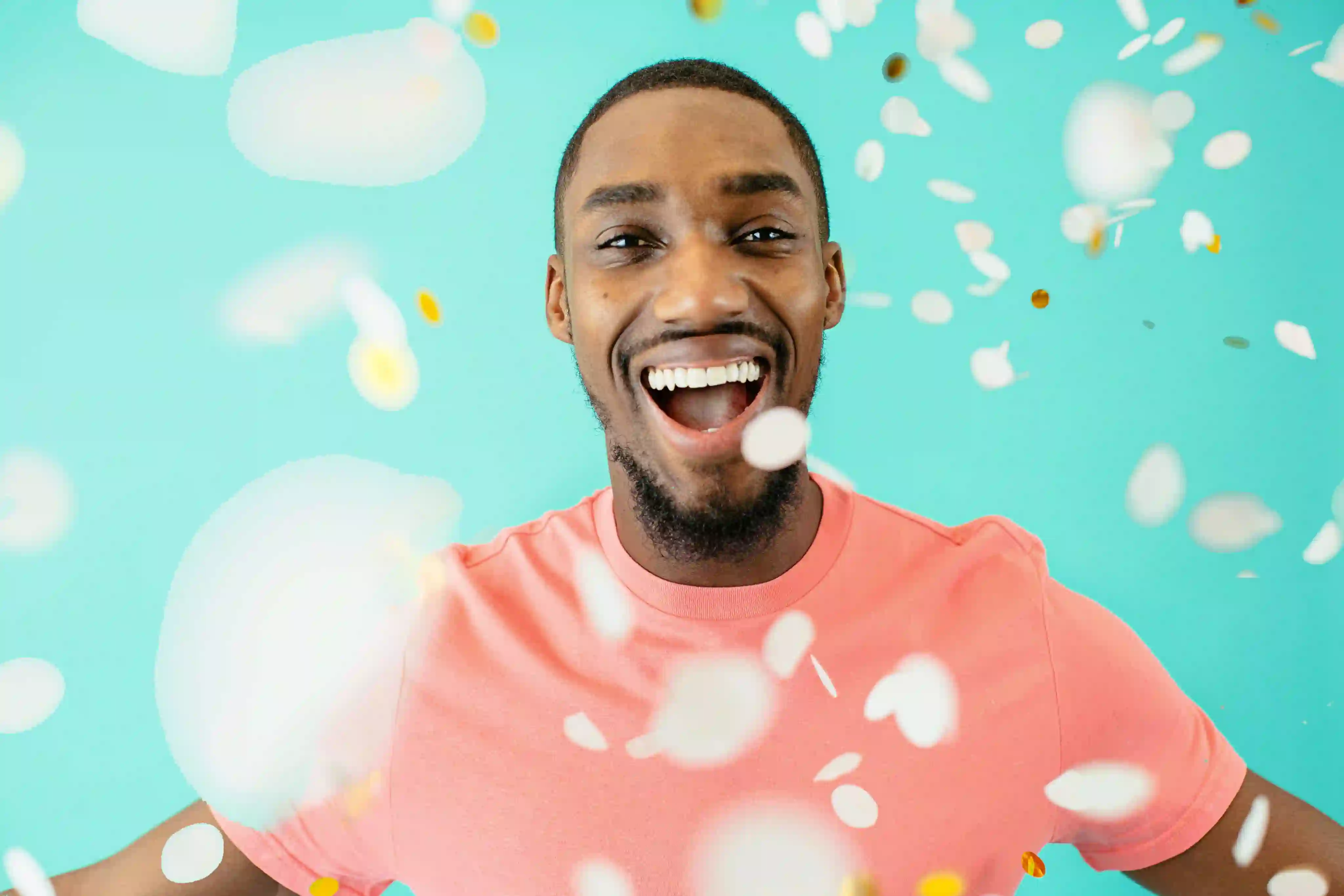 Smiling man in a pink shirt celebrating with falling confetti on a turquoise background