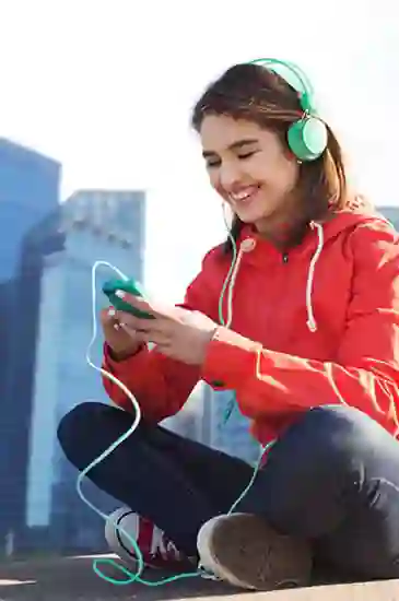 Athletic girl sitting outside, smiling as she listens to music on her phone using over-ear headphones.