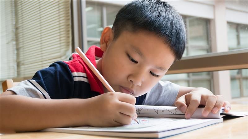 A child concentrates on writing with a pencil on paper. 