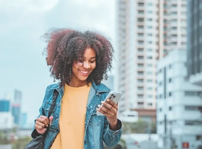 Smiling young woman in denim jacket using smartphone outdoors in the city.