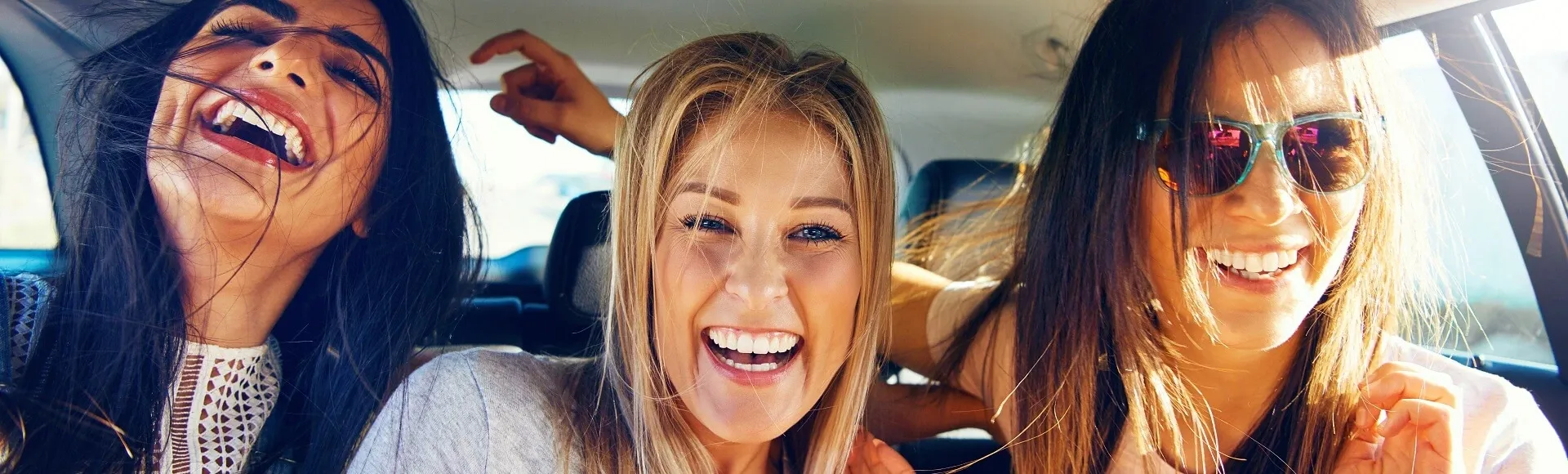Friends laughing together during a road trip inside a car.