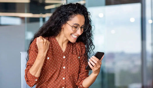 Happy woman celebrating with her phone in hands 