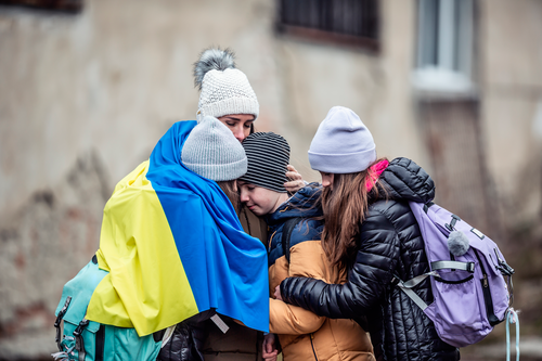 Family embracing outdoors with Ukrainian flag draped around them in a moment of support and solidarity
