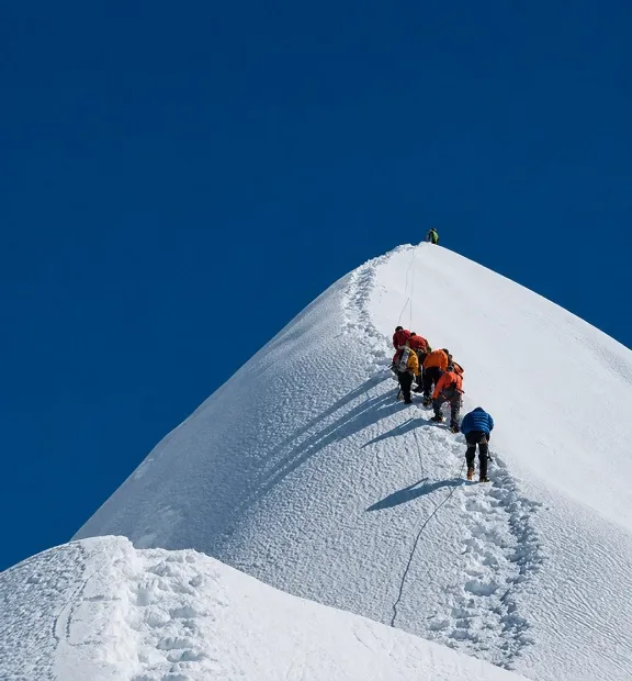 Team of climbers ascending a snowy mountain ridge under a clear blue sky.