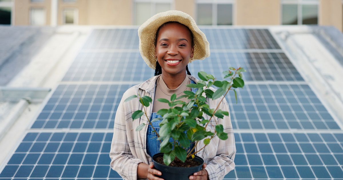 Smiling African woman holding a plant in front of several solar energy panels