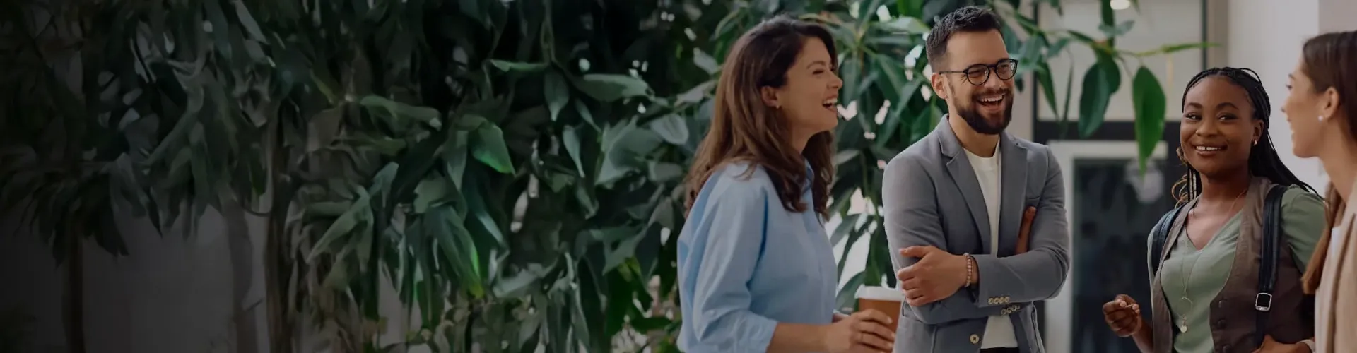 Group of employees talking and laughing in a modern, tree-lined office