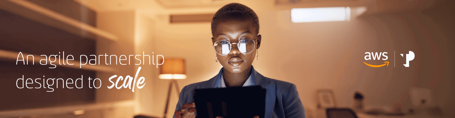 Young African woman wearing glasses uses an iPad in a warmly lit room.