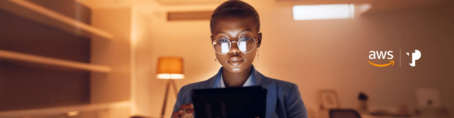 Young African woman wearing glasses uses an iPad in a warmly lit room.