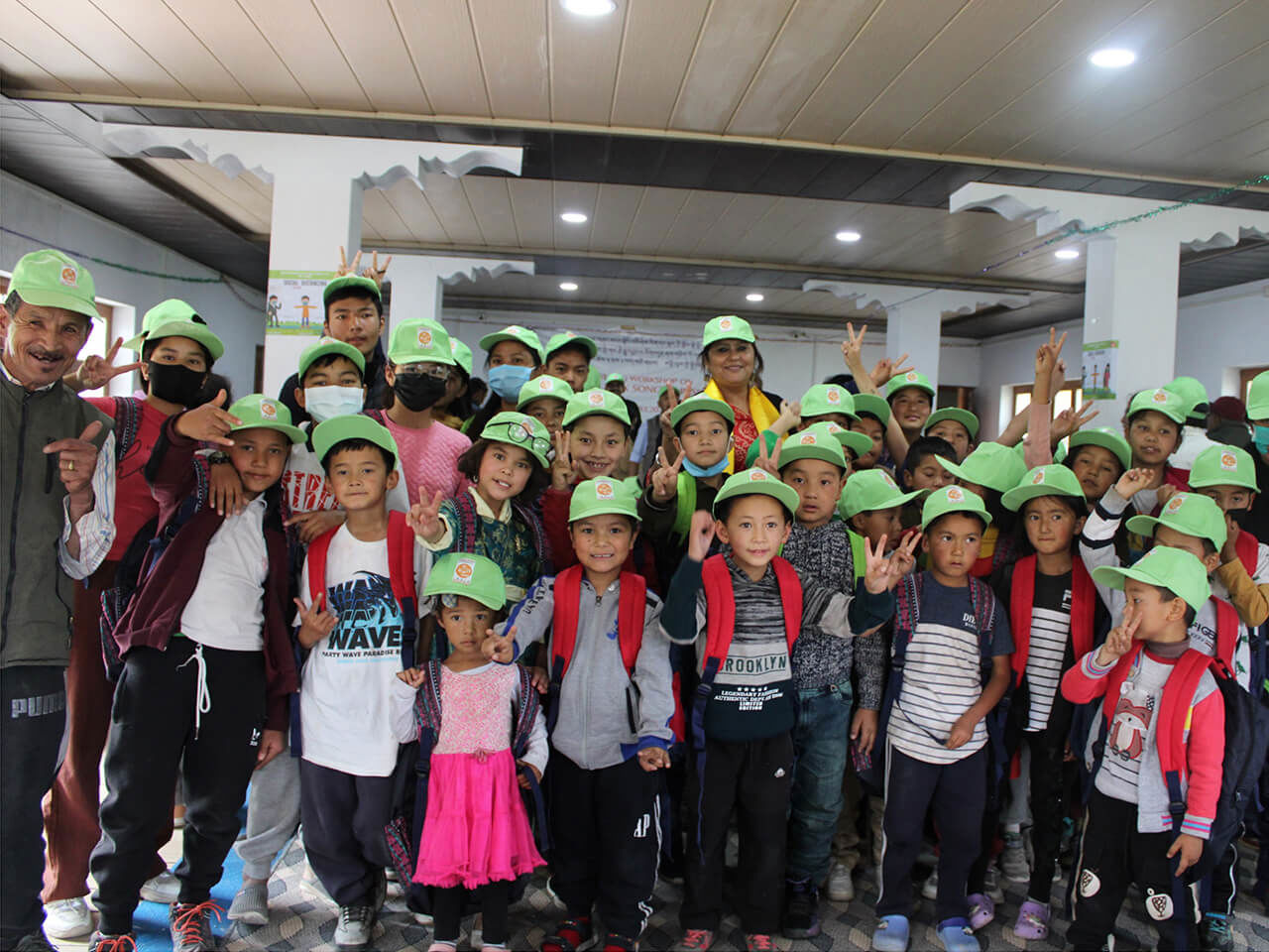 Group of school children wearing green caps and red scarves posing indoors with teachers during an educational event or awareness campaign.