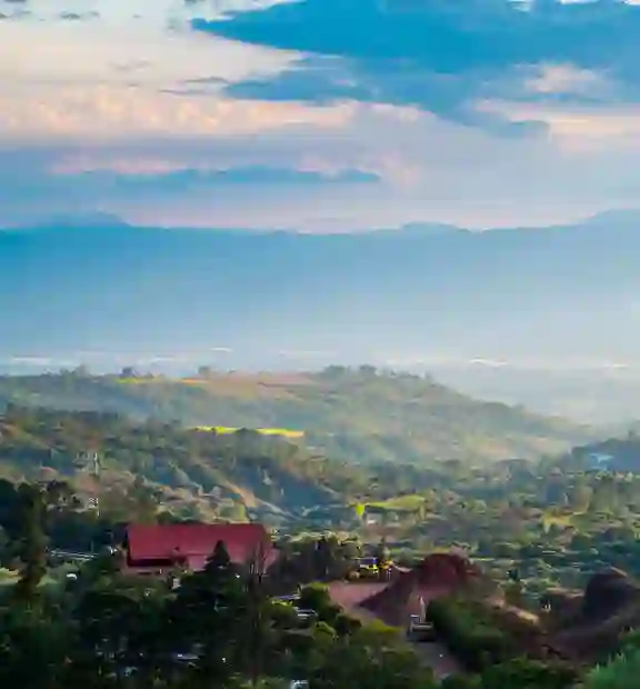 Distant rolling hills extend under a vast sky with scattered clouds, as red-roofed buildings nestle among trees in the lower foreground.