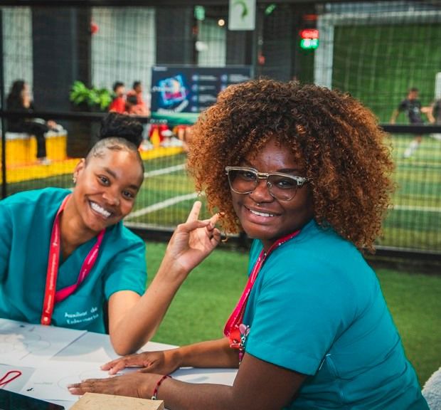 Two Black women smiling and waving to the camera in a relaxed corporate setting.