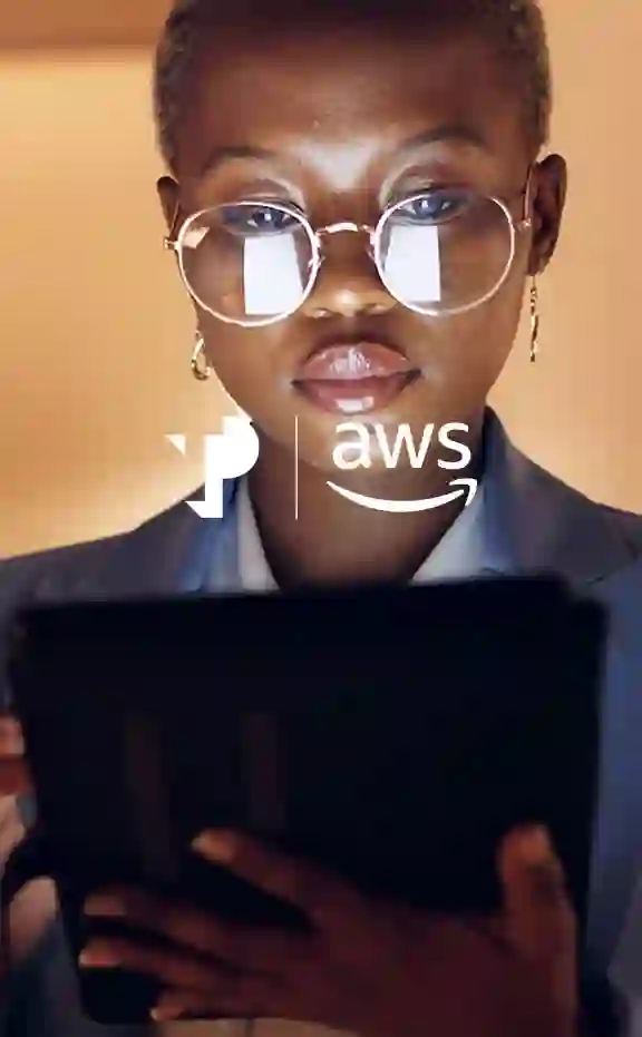 Person wearing glasses, holding a tablet, is illuminated by screen light; logos “TP” and “aws” are overlaid on the image. Background features warm lighting.