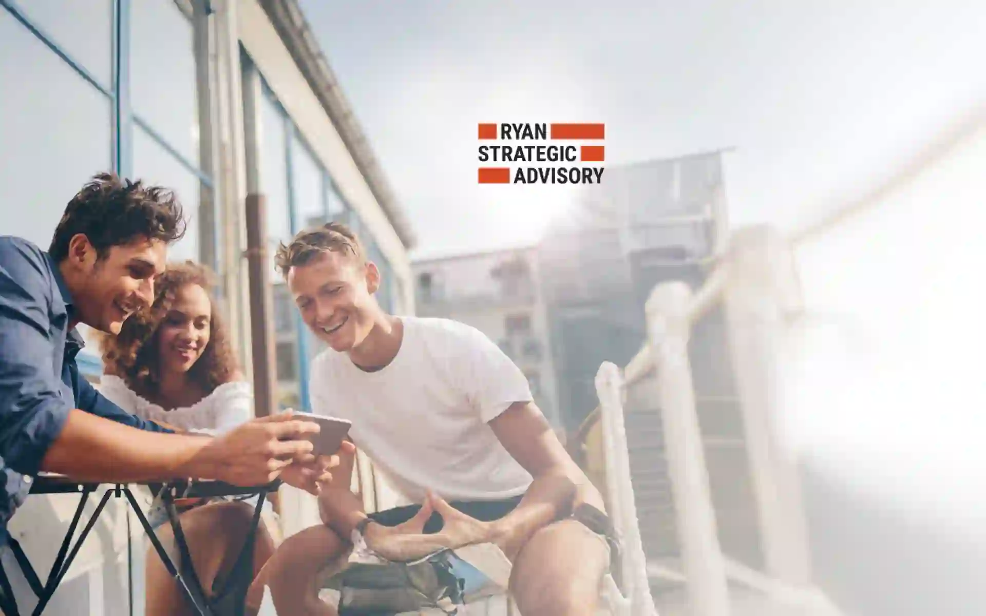 Group of three friends, consisting of two boys and a girl, sitting outdoors watching videos on a cell phone held by one of the men