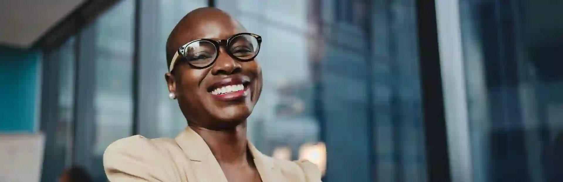  Smiling African businesswoman in elegant attire and glasses, working in a modern office with large glass windows.