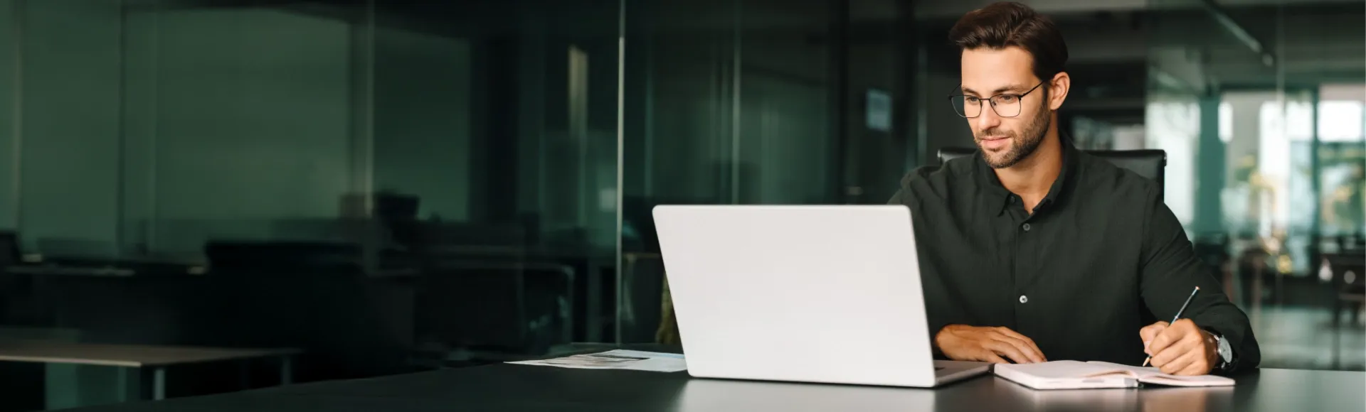 Man focused on a laptop presentation while taking notes in an agenda.