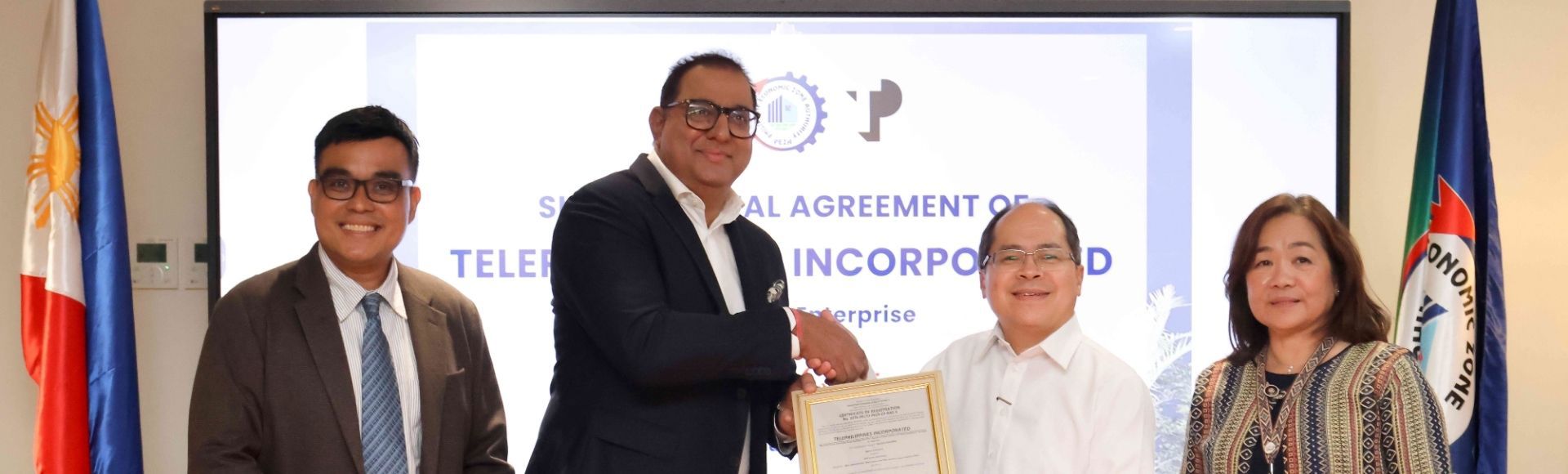 TP in the Philippines CEO Rahul Jolly and PEZA Director General Tereso Panga looking at the camera and shaking hands as PEZA Deputy Director General for Operations Vivian Santos stands beside him