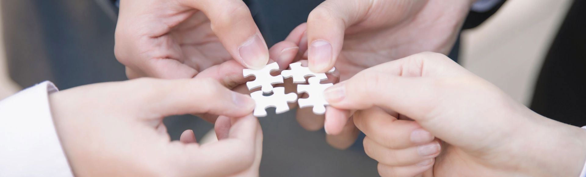 Several hands fit puzzle pieces together to symbolize business cooperation.