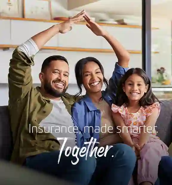 Smiling family sitting on a sofa at home, with parents forming a house gesture, representing TP’s Insurance page.