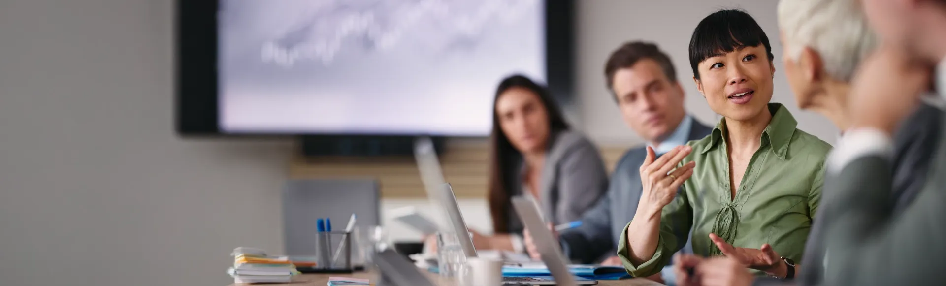 Asian businesswoman leading a meeting with colleagues at a conference table.