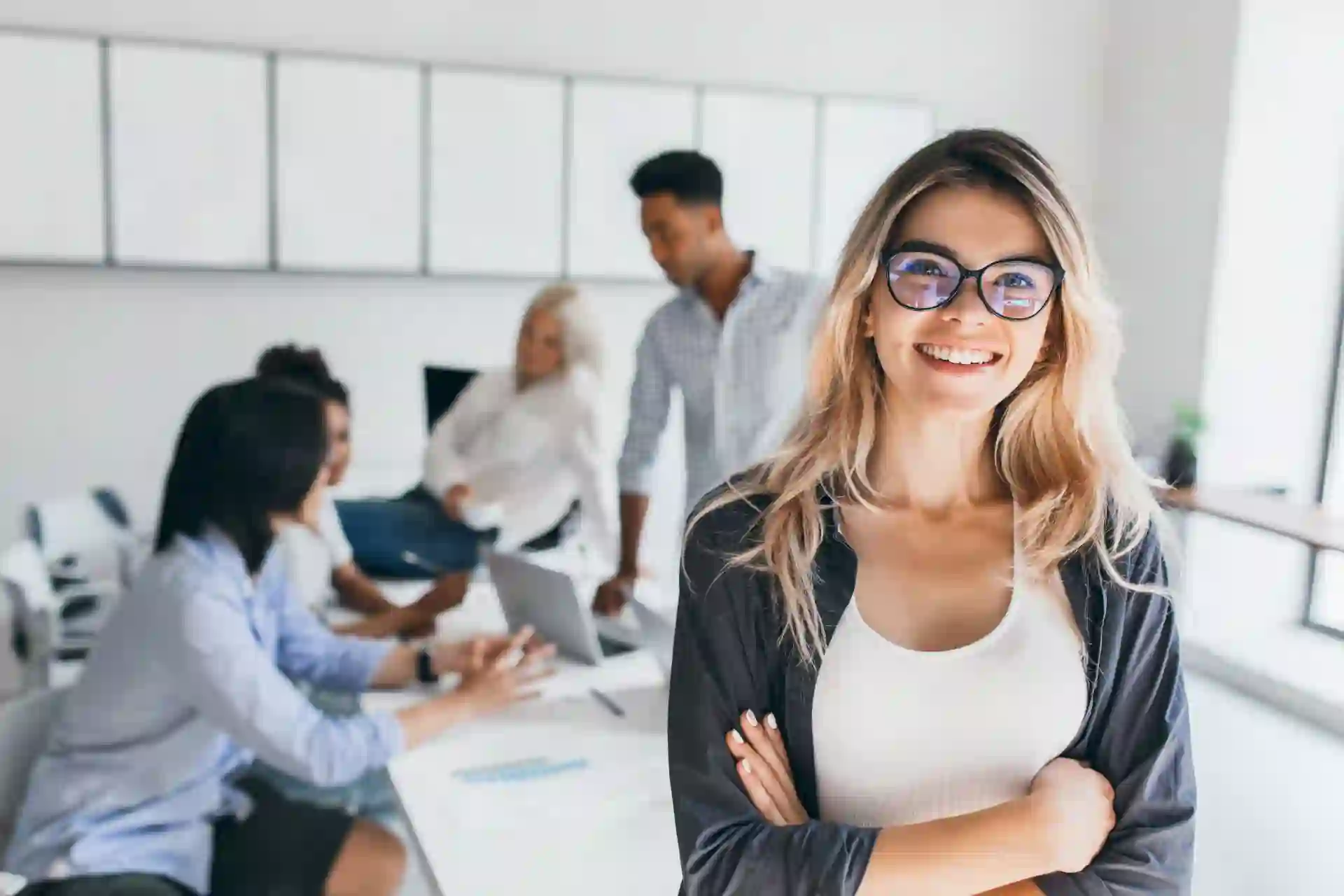 Young smiling businesswoman in front of a desk with her colleagues sitting on a meeting table behind her