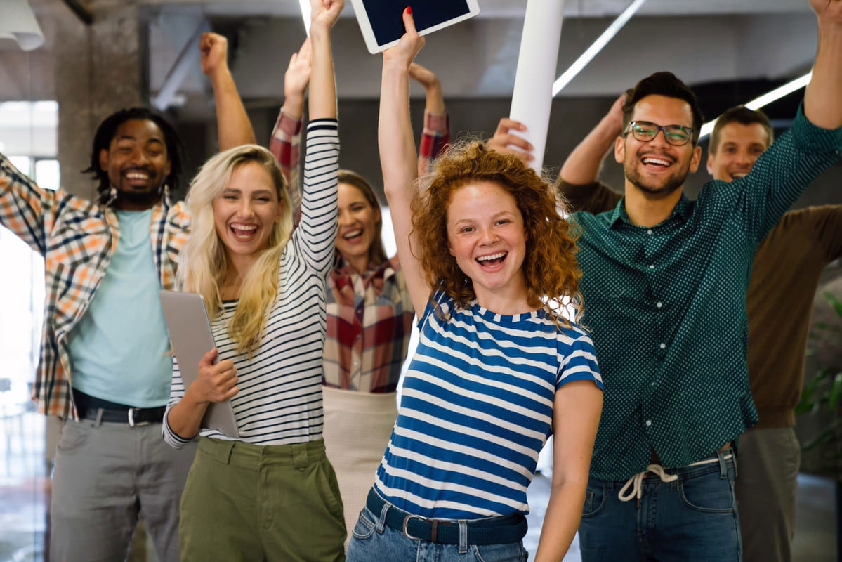 Group of happy employees celebrating a team achievement with hands up
