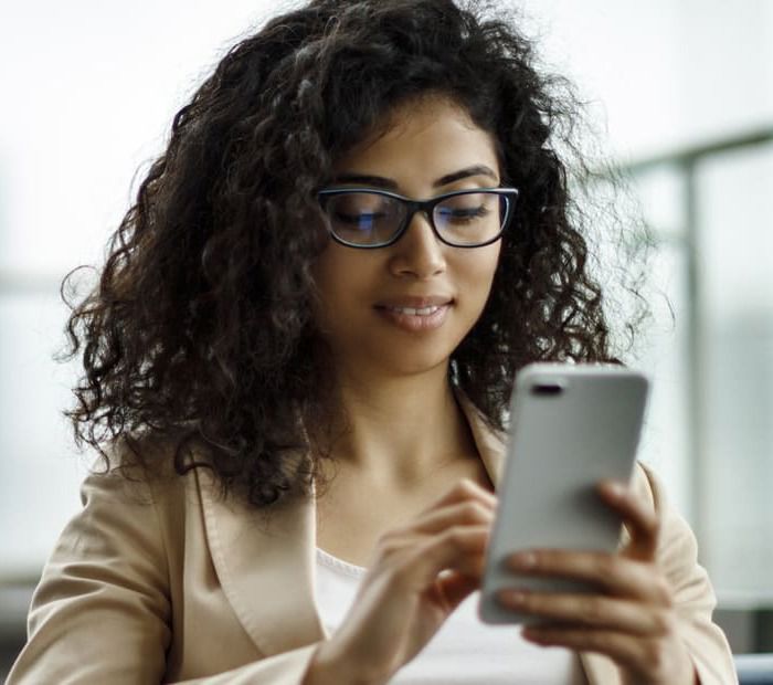 Business woman using her cell phone inside a modern glass walls office