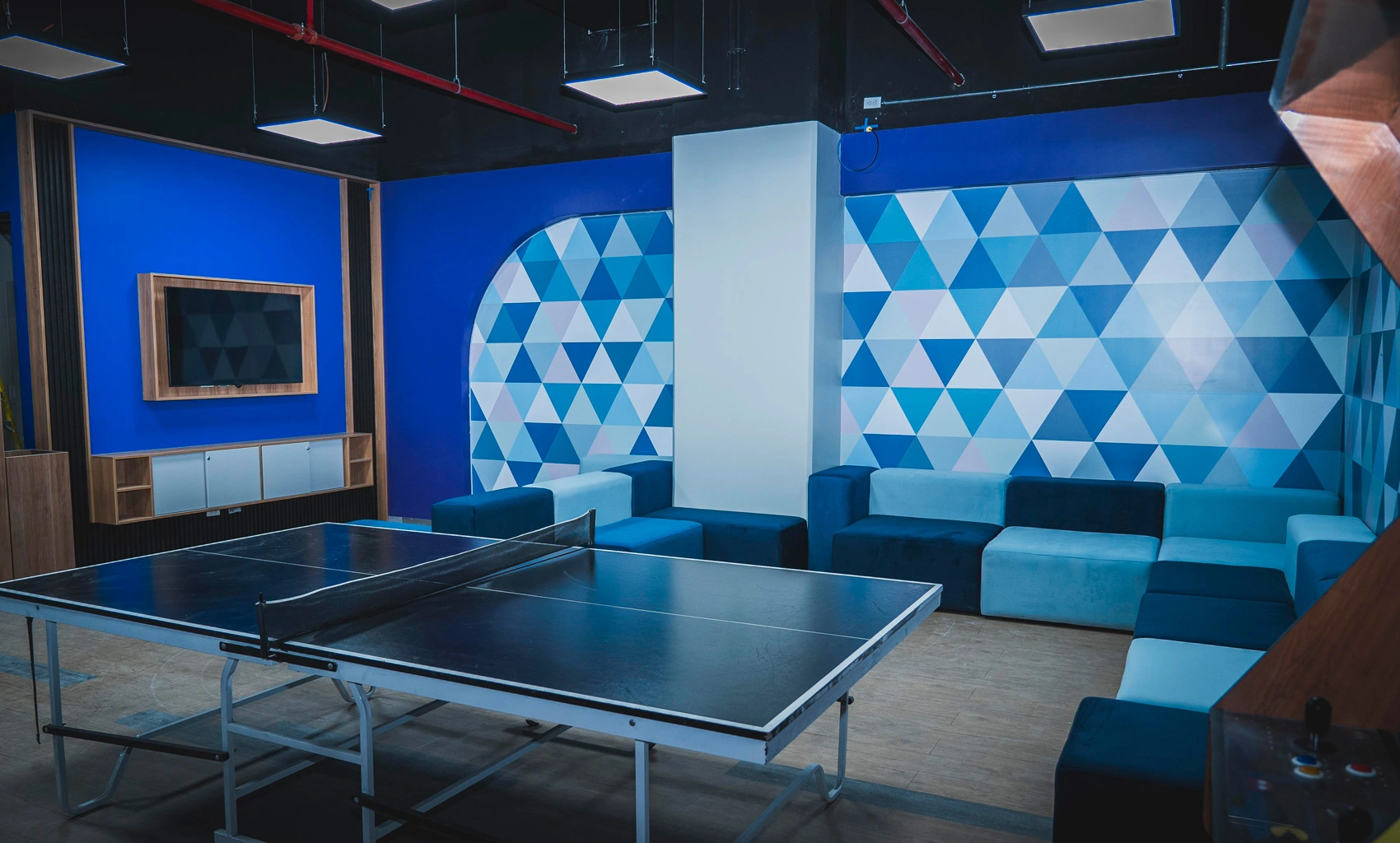 Ping-pong table and lounge with blue geometric walls and couches in a modern recreational space.
