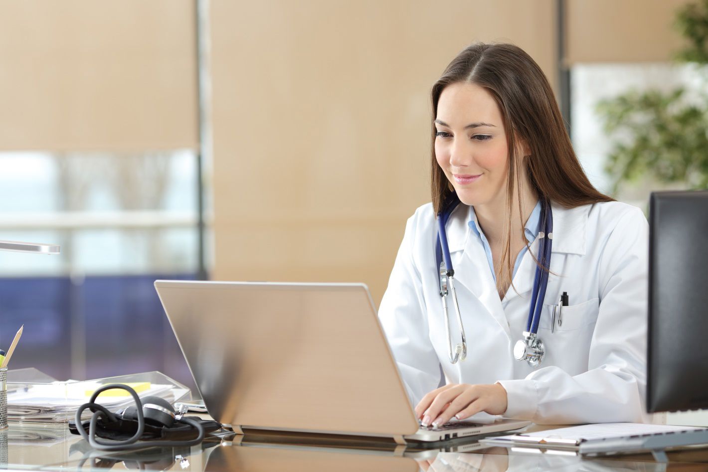 Doctor working on a laptop in a professional office setting.