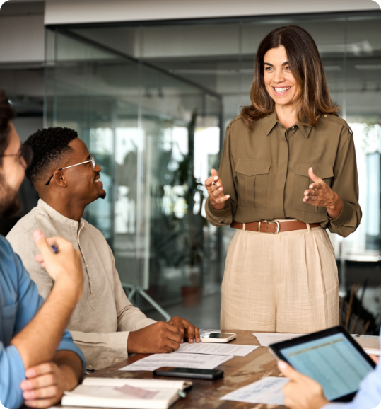 Business team in modern office collaborating on project; woman leads discussion while others engage with tech and ideas.