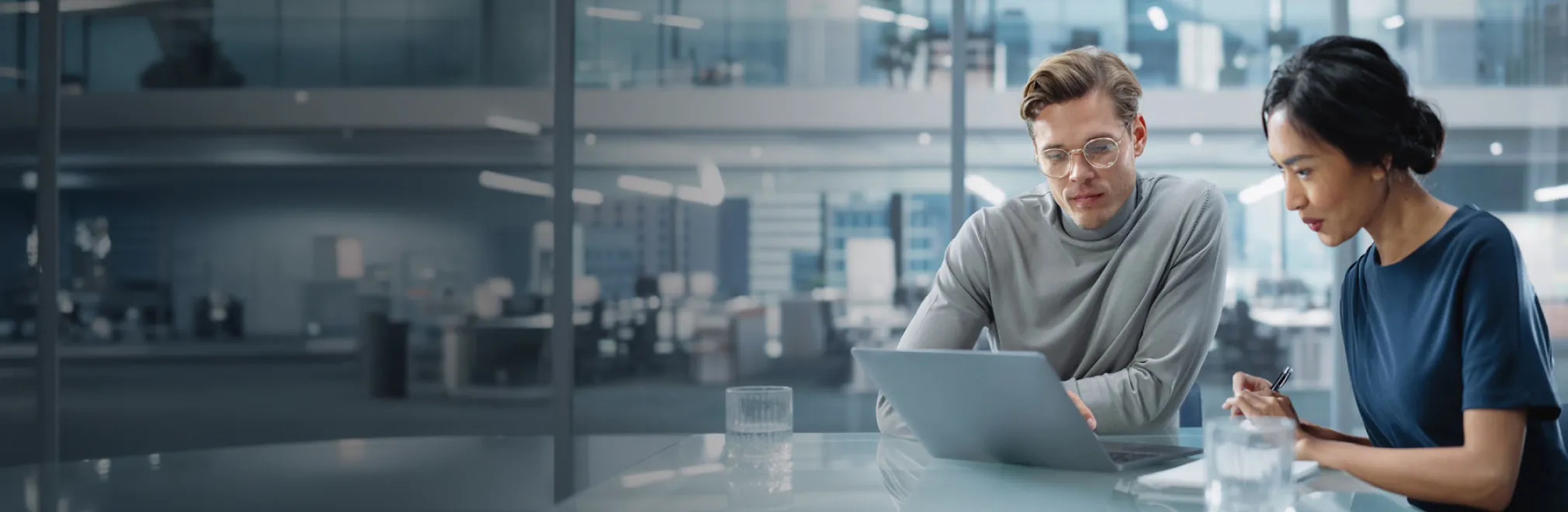 Two professionals reviewing data on a laptop in a modern office.