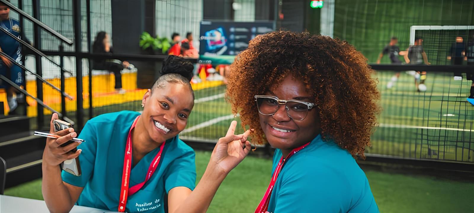 Two Black women smiling and waving to the camera in a relaxed corporate setting.
