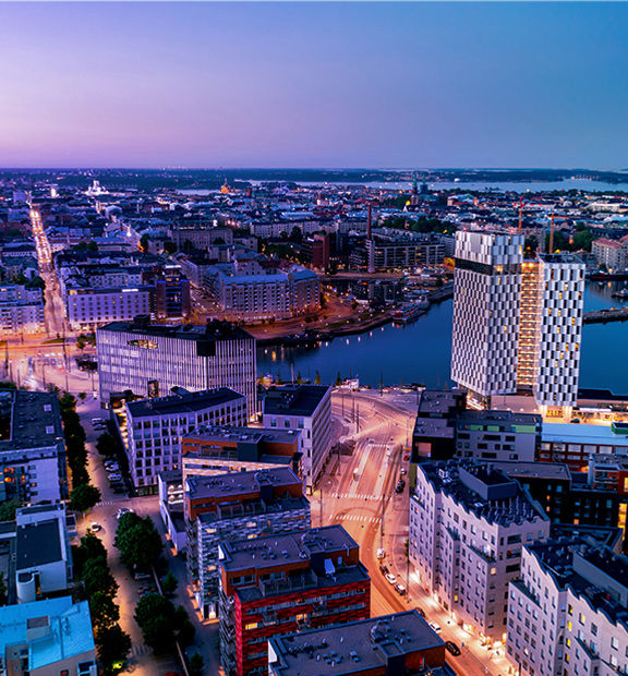 Helsinki cityscape at dusk with illuminated streets and waterfront buildings.