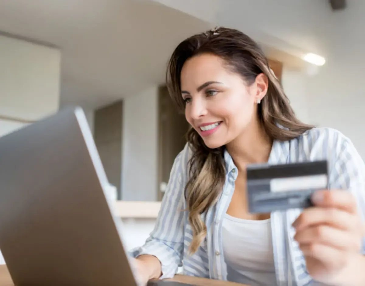 Woman using a laptop while holding a credit card for an online purchase at home.