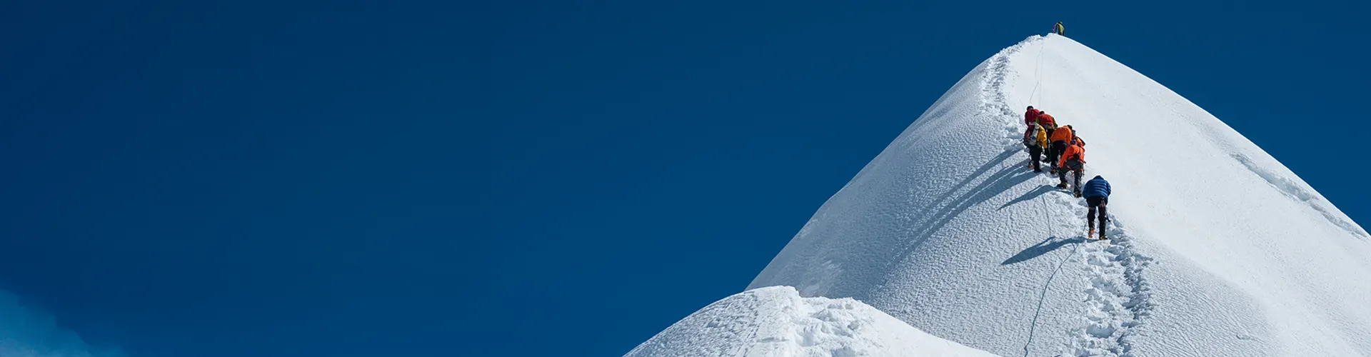 Team of climbers ascending a snowy mountain ridge under a clear blue sky.
