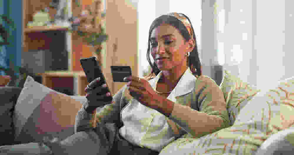 Woman holding her credit card and her cellphone while safely shopping online
