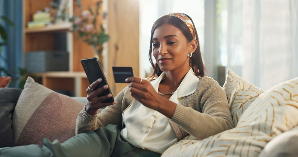 Woman holding her credit card and her cellphone while safely shopping online