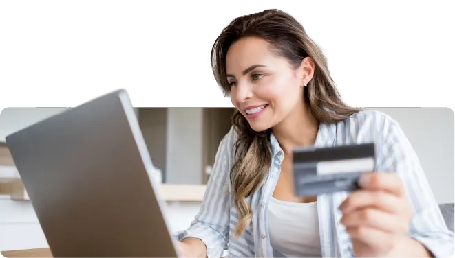 Woman smiling while holding a credit card and smartphone for an online purchase.
