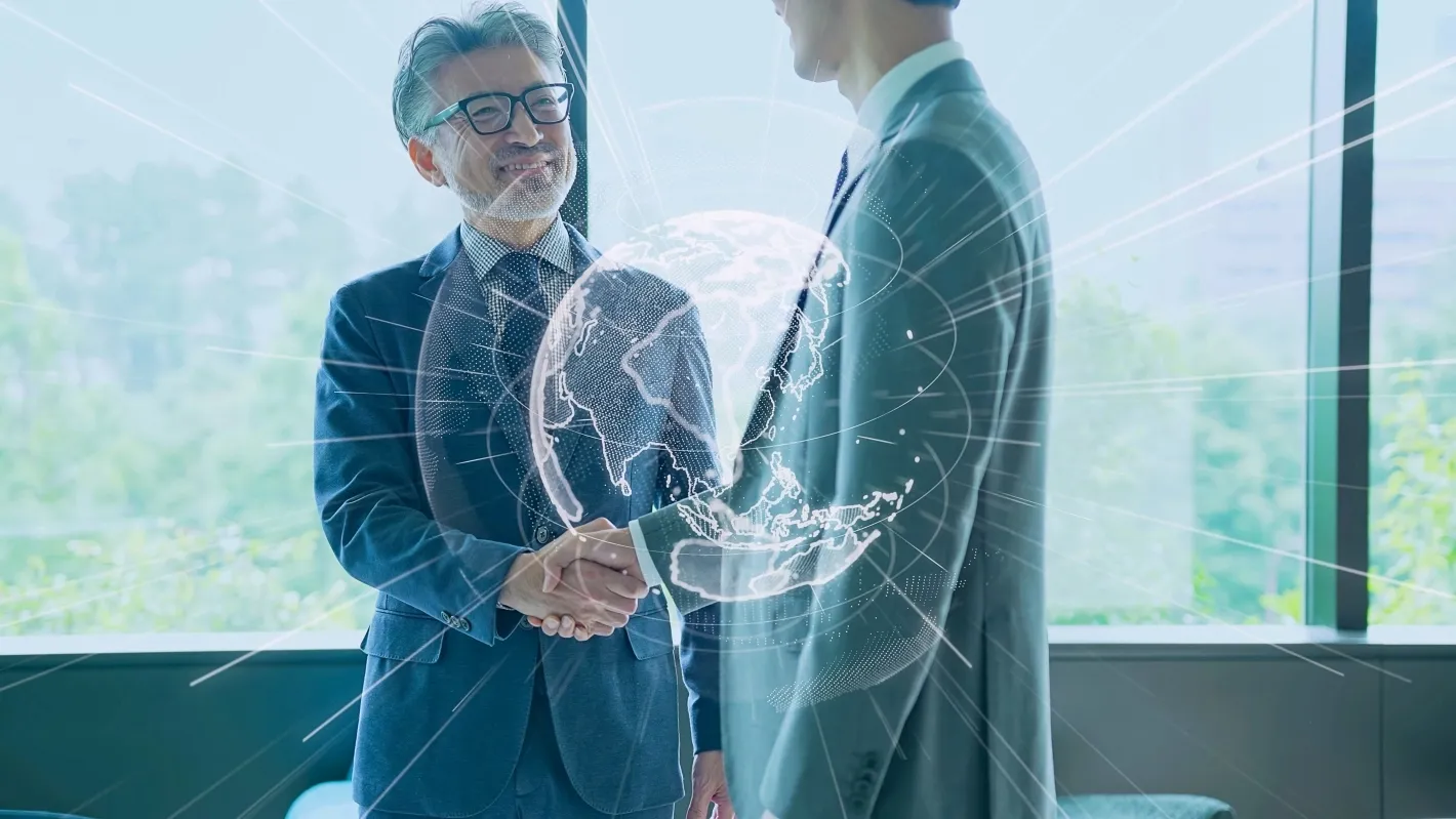 Two business professionals shaking hands, with a digital globe overlay symbolizing global partnership.