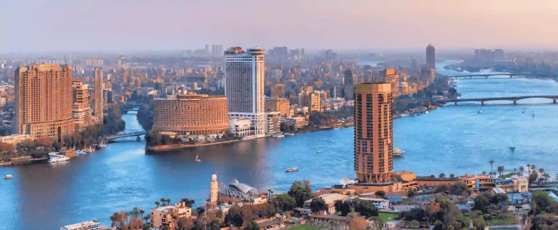 Aerial view of an Egyptian city combining urban sprawl with desert surroundings and glimpses of historic landmarks.