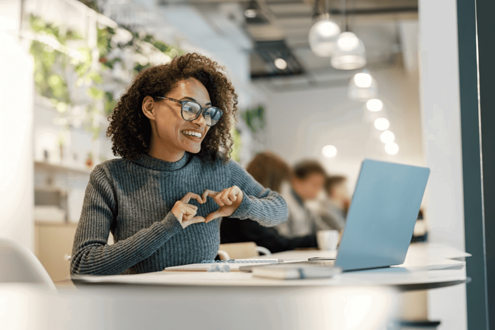 Smiling woman making a heart gesture with her hands at the computer