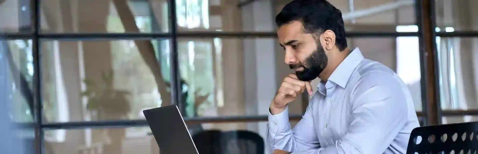 Serious businessman working on his laptop in an office with glass wall
