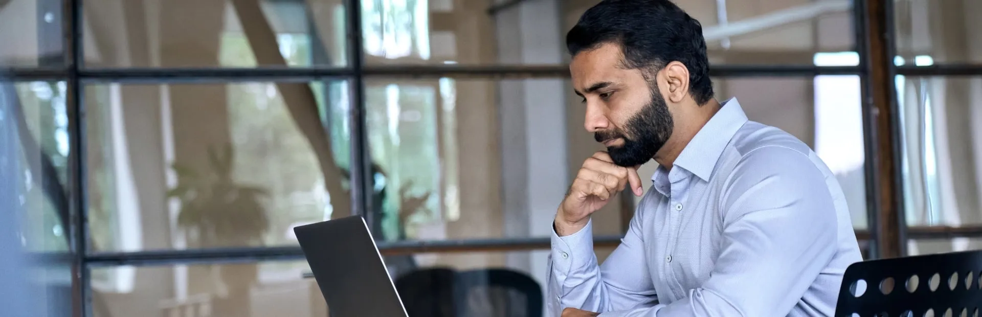 Serious businessman working on his laptop in an office with glass wall