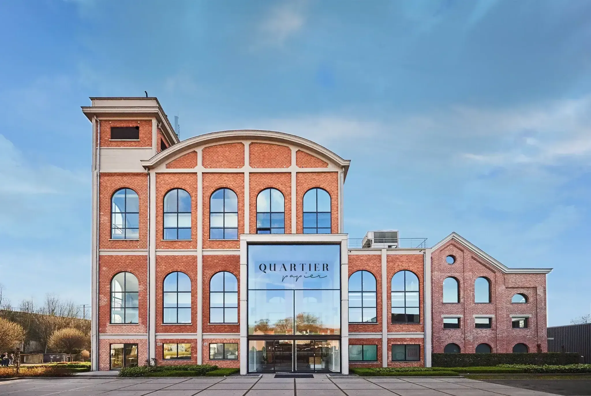 Exterior of the Quartier Papier building with brick façade and large arched windows.