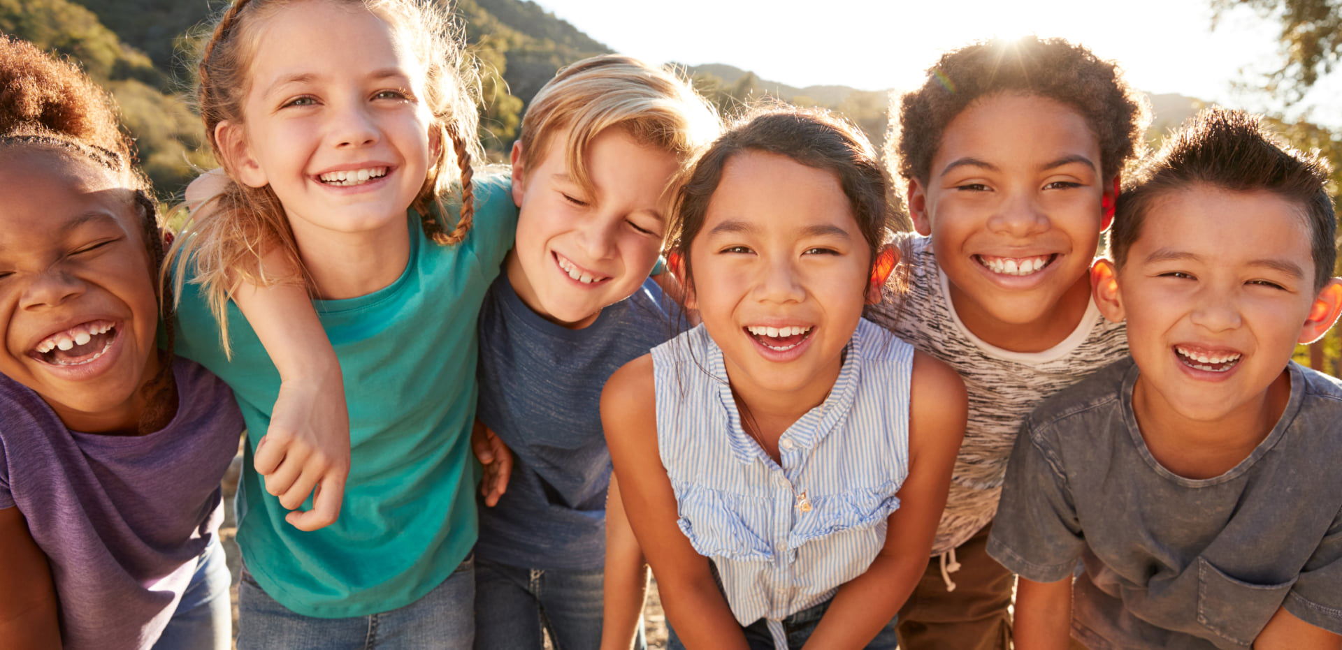 Group of diverse children smiling outdoors with arms around each other.