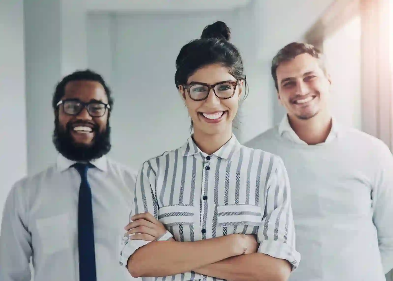 Three smiling professionals standing together indoors, dressed in business casual attire.
