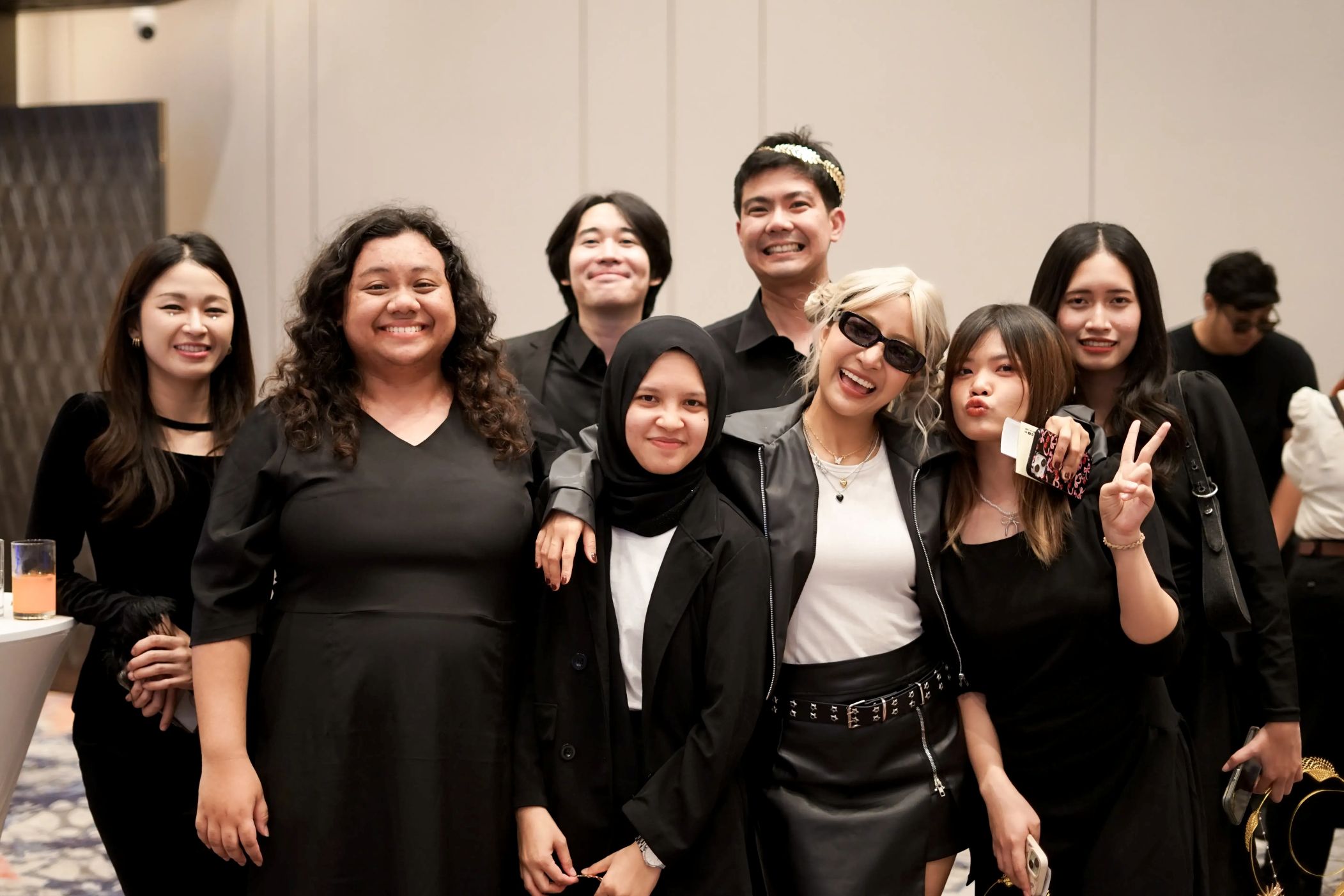 A joyful, diverse group of colleagues in stylish black outfits pose together, sharing smiles and fun moments at a team event.