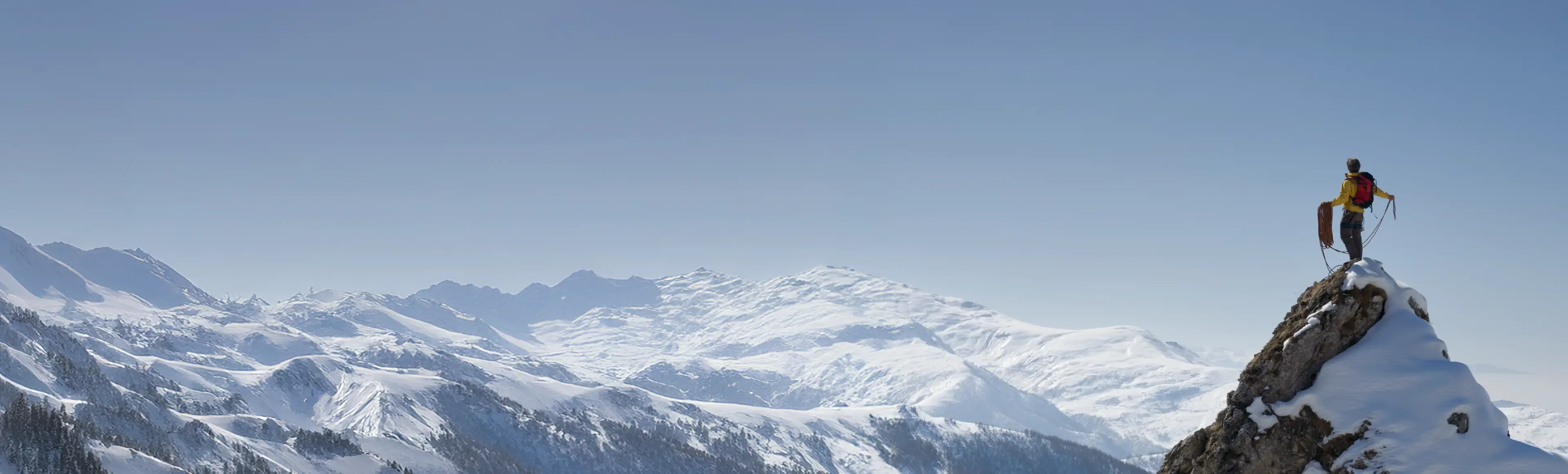 Mountaineer standing on a snowy peak above a mountain range.
