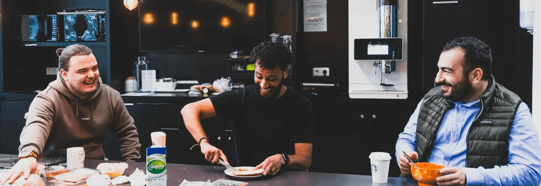 Three guys eating snacks in a kitchen island.