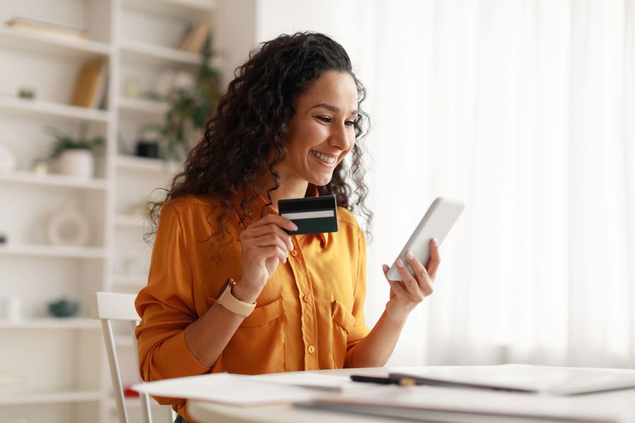 “Woman smiling with relief while holding her credit card and phone, feeling safe using services.