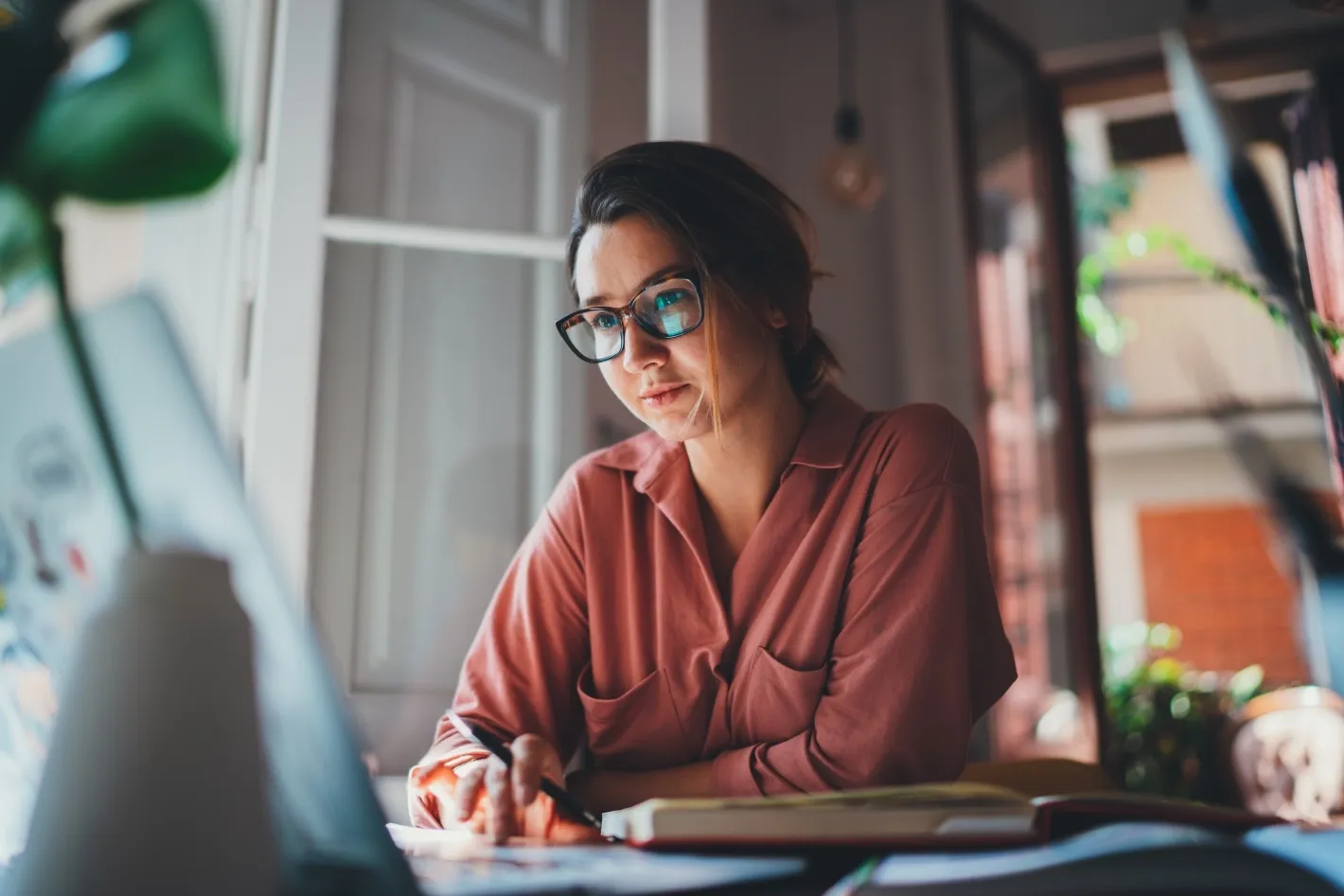 Professional working at a desk, reviewing notes and using a laptop in a focused work environment.